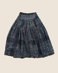 A black tiered skirt with a patchwork design of paisley and floral prints in red, blue, and white, laid flat on a rustic tiled floor.